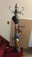 Full view of the black wrought iron hall tree with umbrellas, cane, handbag, and other hanging items.