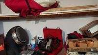 Photo showing Coleman Power Cat heater, Craftsman scroll saw in red case, and boxed candles on shelf.