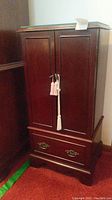 Front view of the closed wooden jewelry armoire with two doors and bottom drawer.