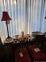 Wide view of all ceramic and decorative items arranged on table under lamp with chairs partially visible.