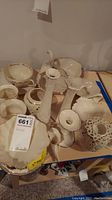 Assorted Lenox porcelain pieces including swan figurine, candle holders, trays, and bowls placed on a cardboard surface. Pieces are white with gold trim.