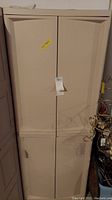 Front view of tall beige plastic cabinet with closed double doors, tagged for auction.