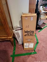 Two cardboard boxes labeled Southern Living at Home Harrison Plate Rack, placed on carpet floor with packaging tape and shipping labels.