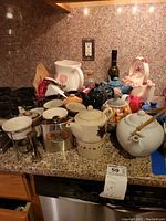 Wide view of the kitchen counter displaying various tea pots, pitcher, hourglass timer, and Japanese porcelain mugs grouped together.