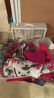 Overview photo showing a white Lasko box fan behind a plastic bin filled with floral patterned throws and various bath mats.