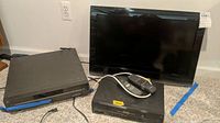 Three electronic devices: Toshiba flat screen TV, Toshiba VHS player, Zenith DVD player with remote on carpeted floor