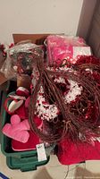 Box filled with Valentine wreaths, tinsel garlands, and heart decorations in red and white colors.