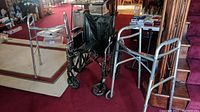 Photo of the wheelchair with both walkers arranged next to each other on red carpet showing front and side views