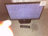 Front view of the LG 25 inch flatscreen television on stand with remote placed in front, screen displaying static.