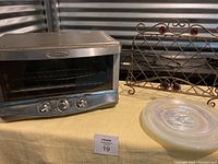 Calphalon toaster oven, metal cookbook stand with red glass accents, and four iridescent plates shown on shelf.
