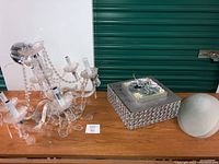 Photo showing six bulb crystal chandelier with decorative hanging crystals, square decorative ceiling light, and two oval glass ceiling fixtures on table.
