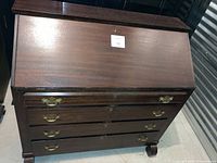 Front view of cherry-colored solid wood secretary desk with drop-front closed and three large drawers with brass handles