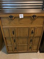 Full front view of tall wooden chest of drawers with multiple drawers and ornate metal handles, faux leather top visible.