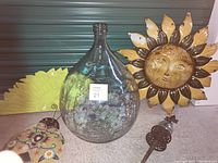 Wide view of all lot items including large glass jug with sea glass, large tins sun and additional garden-themed metal decor items.