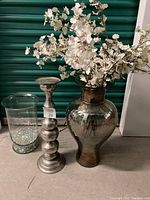Wide view showing all three items: two vases and one candlestick, with flowers in larger vase and pellets in smaller vase.