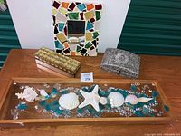 Full view of all items in lot on wood table: sea glass mirror, two decorative boxes and hanging shell decoration