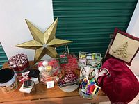 Full view of Christmas decoration lot, including large gold-tone star, red decorative pillow, holiday tins, basket, and celebration hats/noisemakers.