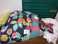 Quilted bedspread and pillows arranged with colorful floral print and lime green decorative pillow on wooden surface under green storage door.