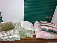 Lot showing stacked quilts, pillow shams, and decorative pillows on wooden table.