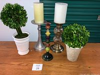 Front view of tabletop decorative items showing two faux boxwood plants and three different styled candleholders.