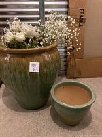 Photo of two ceramic planters: XXL with artificial white flowers inside and a smaller planter next to it, placed on floor.