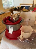 Overall lot showing stacked red baking pans, plastic measuring cup, cookie cutters, and cake carrier.