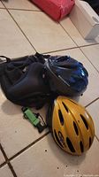 Two bike helmets (Schwinn black, Giro yellow), black bike saddle bag, padded gel bike seat cover on tiled floor