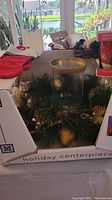 Overview of holiday centerpiece components including candle holder, pine branches, and includes other decor like mini stocking and mug in background