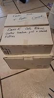 Stacked white cardboard boxes labeled as Dansk fondue dish, heater, center fondue pot, stand, and extras, with handwritten notes on box tops.