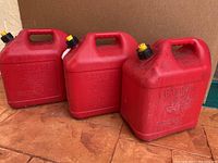 Three red 5-gallon gasoline containers with yellow and black caps, showing general wear and dirt.