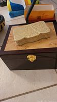 Dark polished wooden jewelry box with gold latch, showing top surface and part of sides