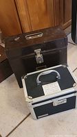 Photo showing two lock boxes, one large dark brown metal box and one smaller black and silver box with combination lock and handle.