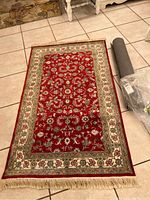 Full view of the Persian design faux silk rug with visible fringe and rolled rug pad beside it.