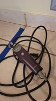 Full view of the purple Oster Protégé pet clipper with a black power cord attached, resting on a tiled floor.