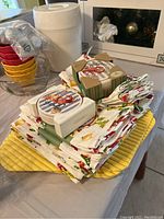 Folded cloth napkins and placemats stacked with two sets of round coasters in wooden holders on top.