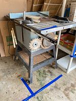 Full view of the Delta 10" table saw with metal stand on wheels, showing attached side blades and black blade guard.