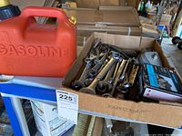 Cardboard box with assorted hand tools including wrenches and pliers, next to a red gas can