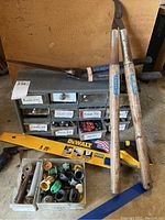 Photo showing sorting box with labeled compartments and assorted small hardware parts, along with hand tools including pruners and saw handles