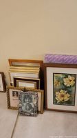 Several photo and wall art frames grouped on floor, including wood, metal and ceramic finishes