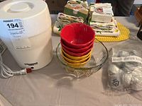 Yogourmet yogurt maker, stacked red and yellow melamine dessert bowls, clear glass bowl, and various items in the background on table.