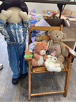 Wide-angle view of the wooden child-sized chair with four stuffed toys seated and the large decorative cloth doll standing next to it, showing the overall lot contents.