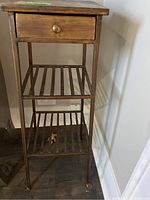 Full view of metal decorative side table showing drawer, two slatted shelves, and overall condition.