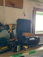 Photo showing Dewalt cordless drill, Dewalt battery charger, and Dewalt laser pointer in a black carrying case next to a wooden shelf.
