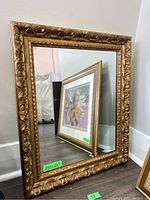 Angled view of the framed mirror showing the glass reflection and ornate gold frame with labeled size 25x21 inches.