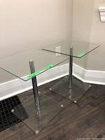 Pair of glass end tables showing top and base with metal cylindrical support column.