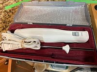 Electric knife with white handle and blades, cord wrapped beside it inside red lined case.