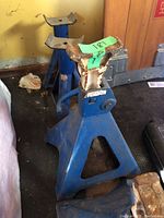 Set of 4 blue 5-ton jack stands placed in garage corner, showing two stands with rusted curved saddle plate and two with flat top saddle.