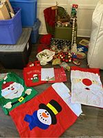 Overview of Christmas gift bags and assorted decorations placed on the floor near storage bins