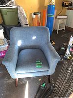 Front angle view of the blue fabric living room chair, showing rounded armrests and wooden legs. Chair is placed in a garage surrounded by various items.