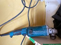 Full side view of used Makita angle grinder showing blue body, power cord, and grinder head.